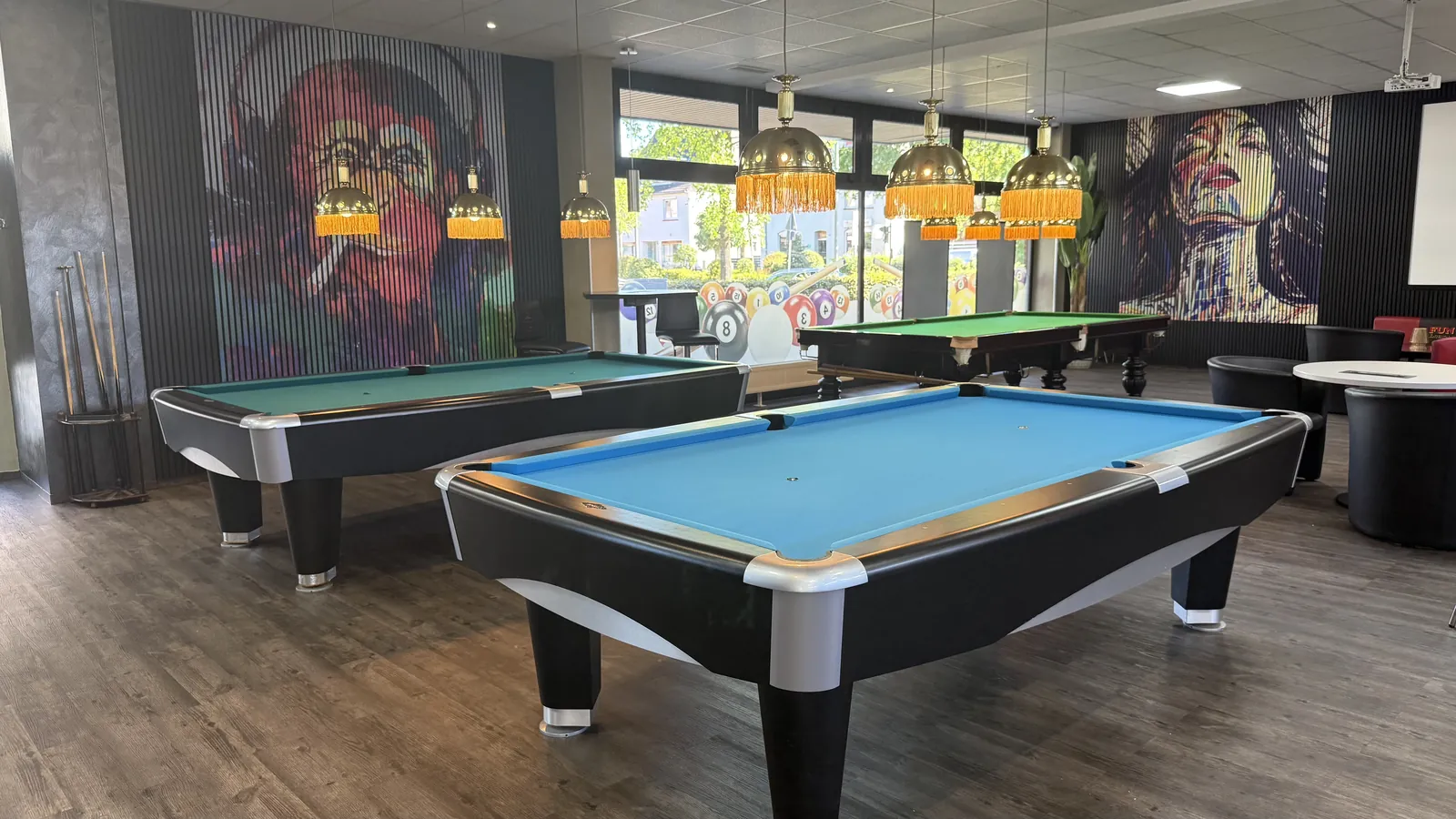 Zwei Pooltische mit blauem Tuch unter goldenen Fransenlampen in der Players Lounge Voerde