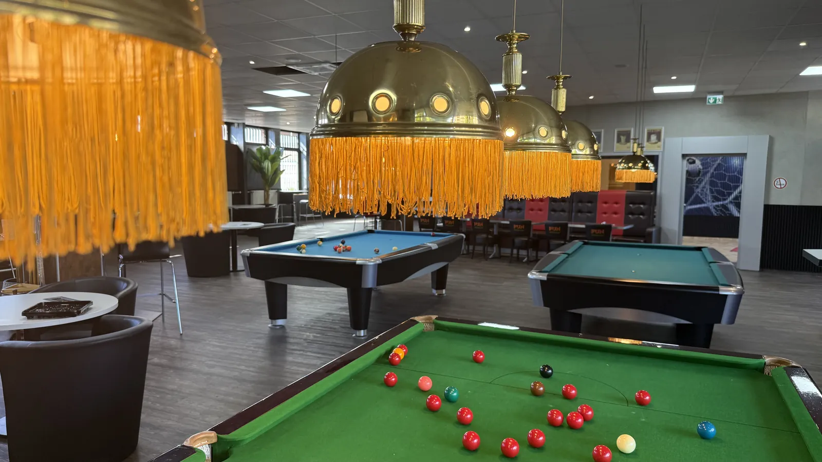 Saal der Players Lounge Voerde mit Snookertisch im Vordergrund, zwei Pooltischen und goldenen Fransenlampen