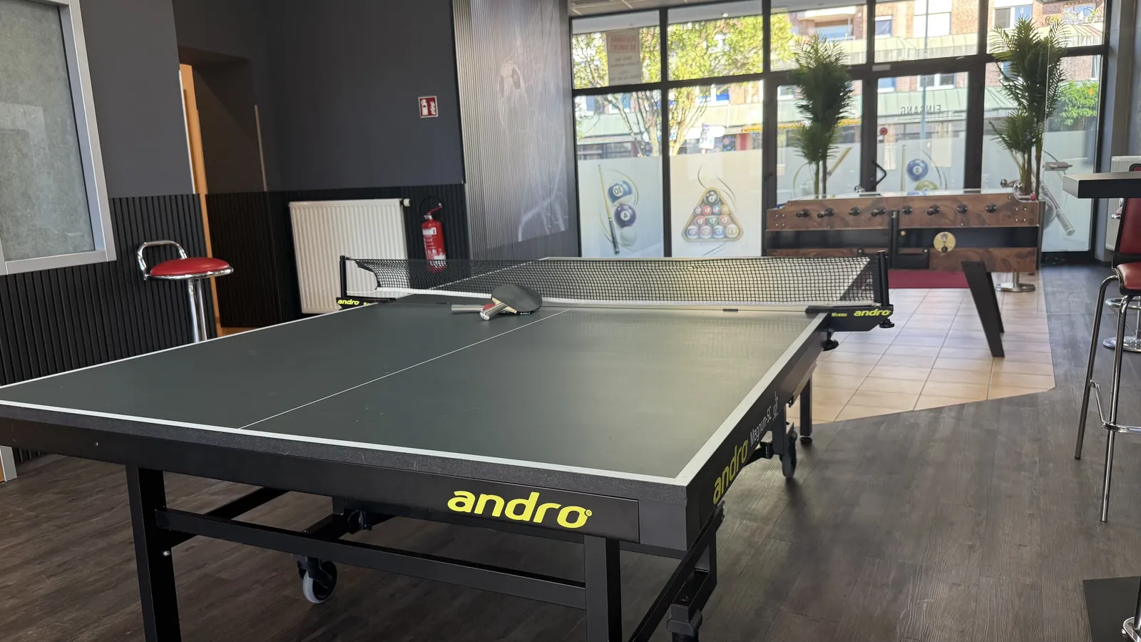 Aufgebaute Tischtennisplatte in der Players Lounge Voerde, dahinter Kicker und Fensterfront